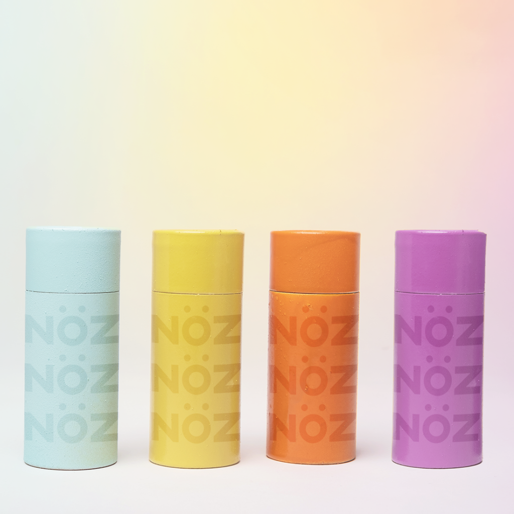 Four sticks of Noz’s reef-safe sunscreen in teal, yellow, orange, and purple