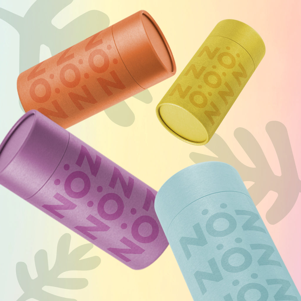 Four sticks of Noz’s reef-safe sunscreen in teal, yellow, orange, and purple floating on a background